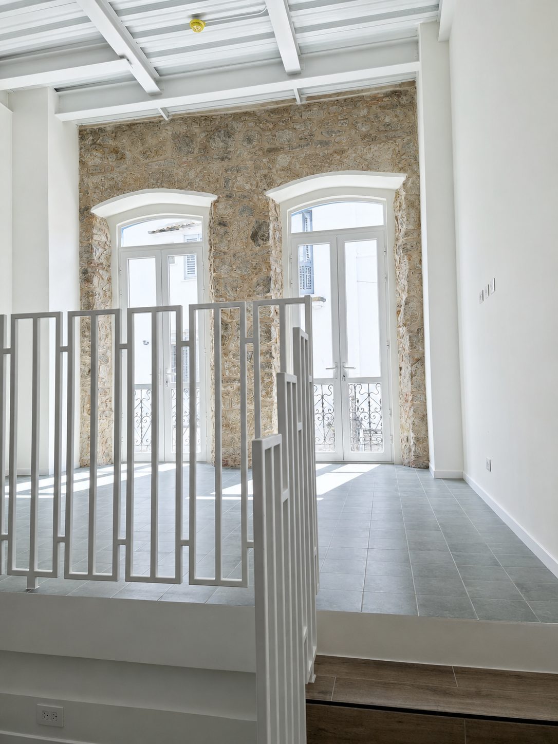Interior tipo loft de Casa Variedades: muro de piedra histórica original, ventanales en arco y baranda de hierro.